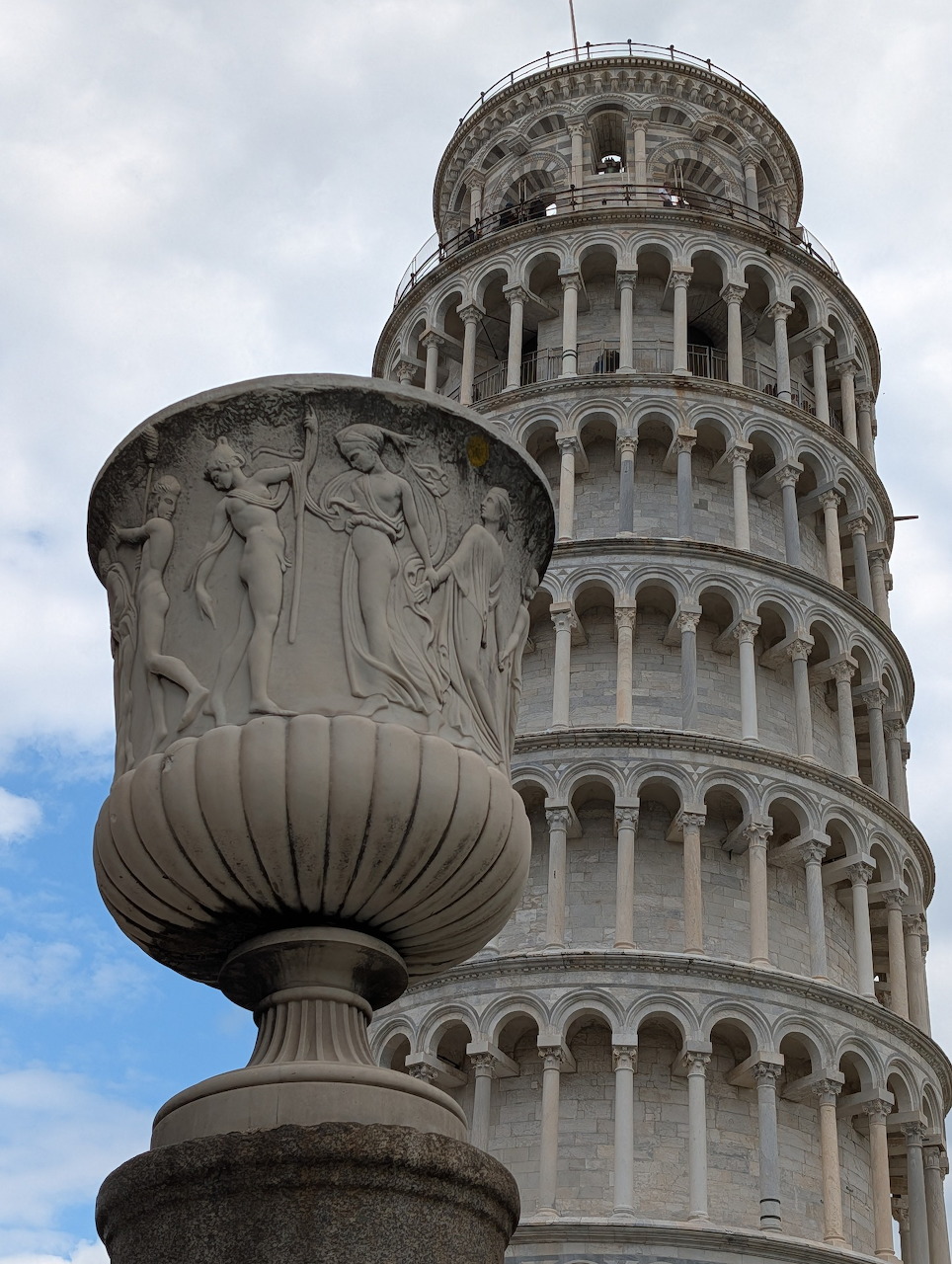 Leaning Tower of Pisa behind a carved stone urn under a cloudy sky