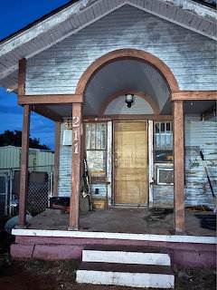 Weathered wooden house with a covered front porch, steps, and peeling paint at dusk