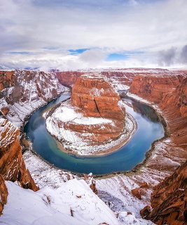 Snow-dusted Horseshoe Bend canyon with turquoise river curving through orange rock formations under cloudy sky