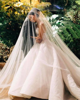 Bride wearing white wedding gown with long flowing veil in garden