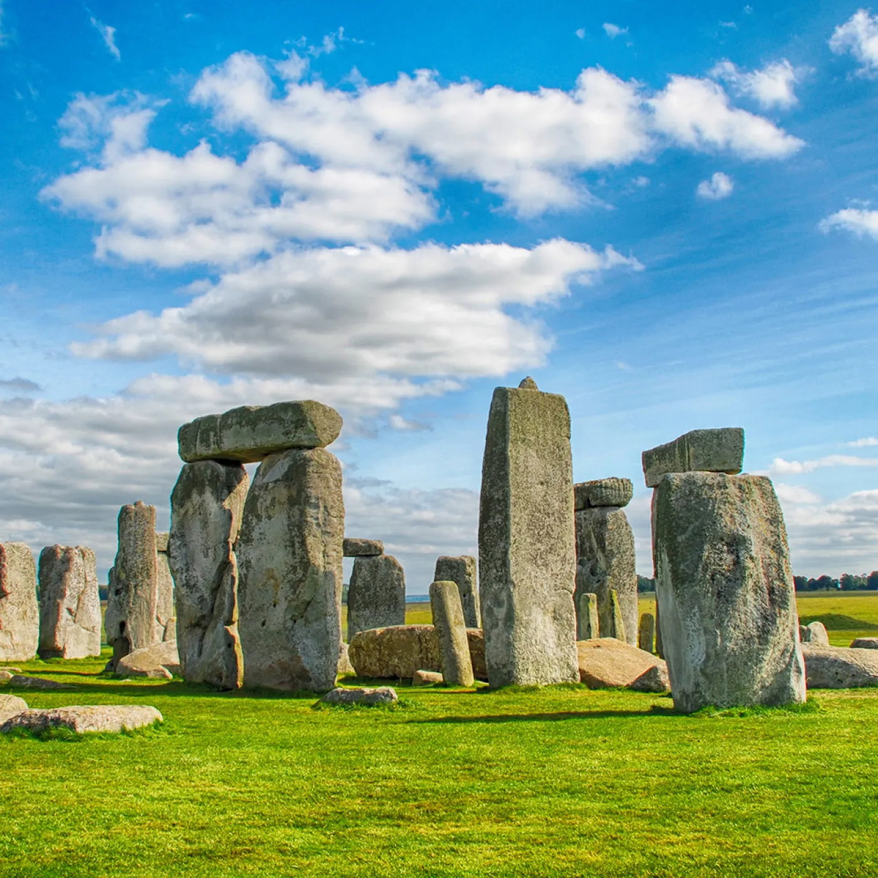 Stonehenge standing stones on a grassy field beneath a blue sky with clouds