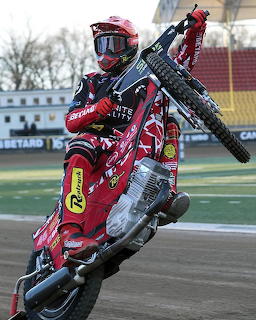 Speedway rider in red gear sliding sideways on motorcycle during race