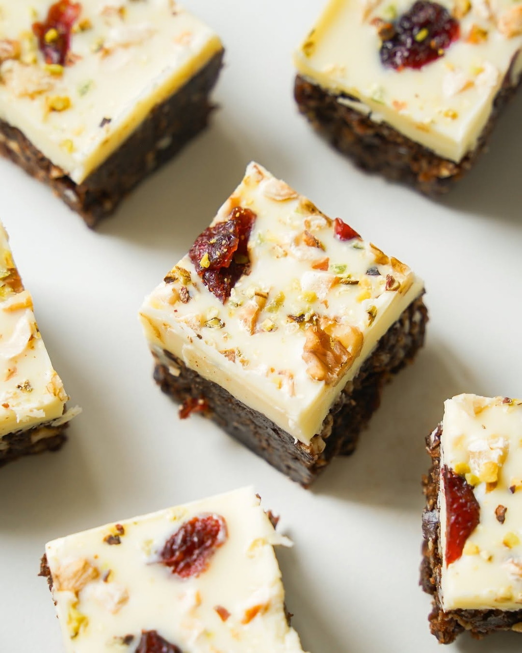 Layered chocolate bars with white chocolate topping, dried cranberries and nuts on a white background