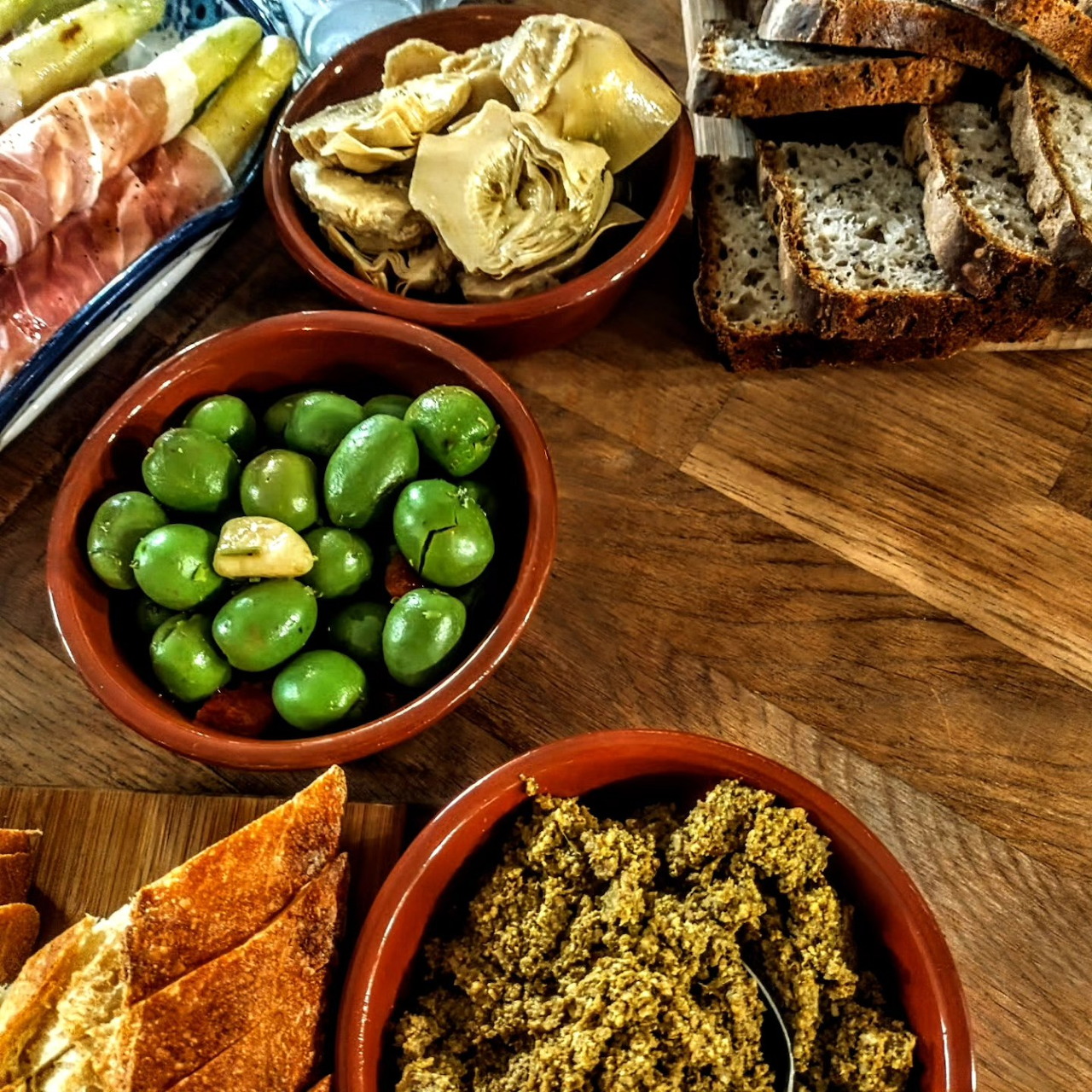 Rustic bread, green olives, artichokes, cured meat, and spread on a wooden table