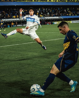 Soccer players contest the ball near the sideline in a stadium match.