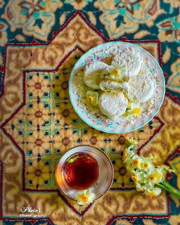 Overhead view of tea in glass cup, plate of powdered pastries, and daffodils on ornate Persian rug