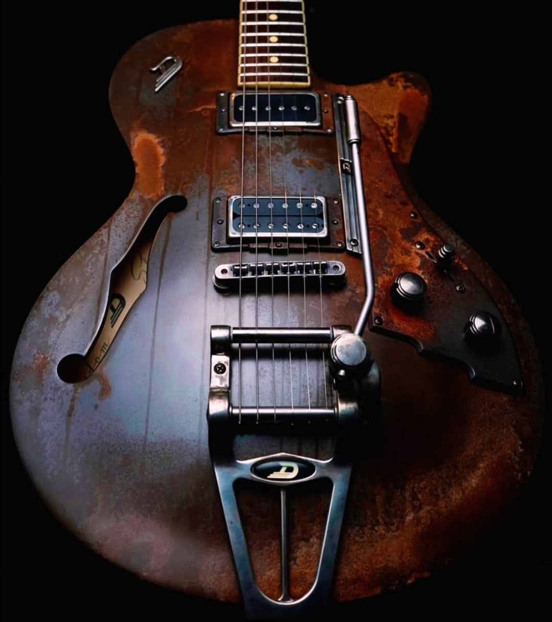 Worn semi-hollow electric guitar with rusted metal body and chrome tailpiece on dark background