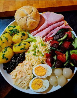 Chef's salad platter with ham, eggs, cheese, vegetables, potatoes and bread rolls on white plate