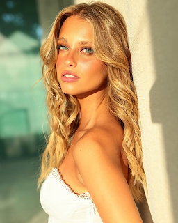 Young blonde woman with wavy hair posing in sunlight wearing a white top