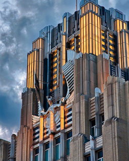 Top of an art deco building with gold and bronze geometric ornamentation against cloudy sky