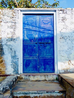 Bright blue door in a worn white wall above stone steps