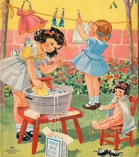 Two young girls washing dolls in a washtub outside, with clothes hanging on a line behind them