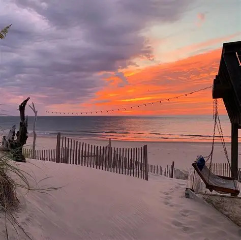 Sandy beach at sunrise with wooden fence and golden sky