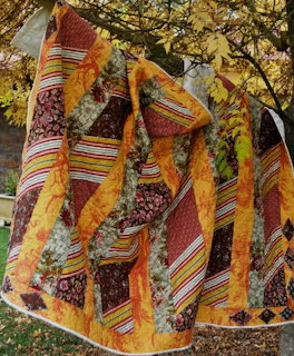 Colorful patchwork quilt with orange, brown, and floral patterns hanging on wooden fence outdoors