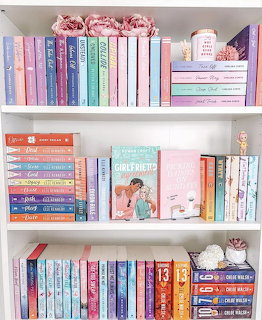Organized bookshelf with colorful books in pink, blue, and pastel shades arranged on white shelves