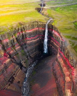 Aerial view of waterfall plunging into colorful layered canyon with surrounding green landscape