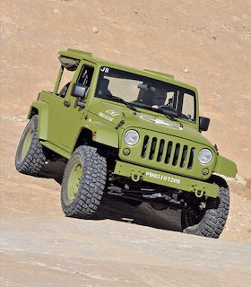 Green Jeep Wrangler J8 pickup truck on rocky desert terrain with sand hill behind