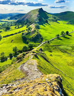 Green rolling hills and rocky ridge of Chrome Hill in the Peak District under a blue sky with clouds