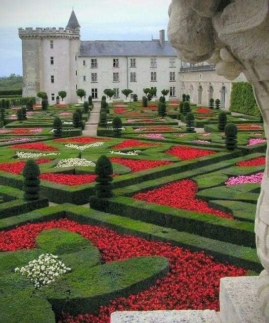 Formal parterre garden with red flowers and sculpted hedges before a white stone château
