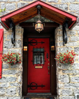 Red front door with ornate iron hardware on a stone building with hanging lantern and red flower boxes