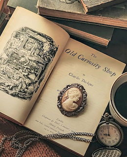 Vintage book The Old Curiosity Shop open with pocket watch and cameo on wooden surface