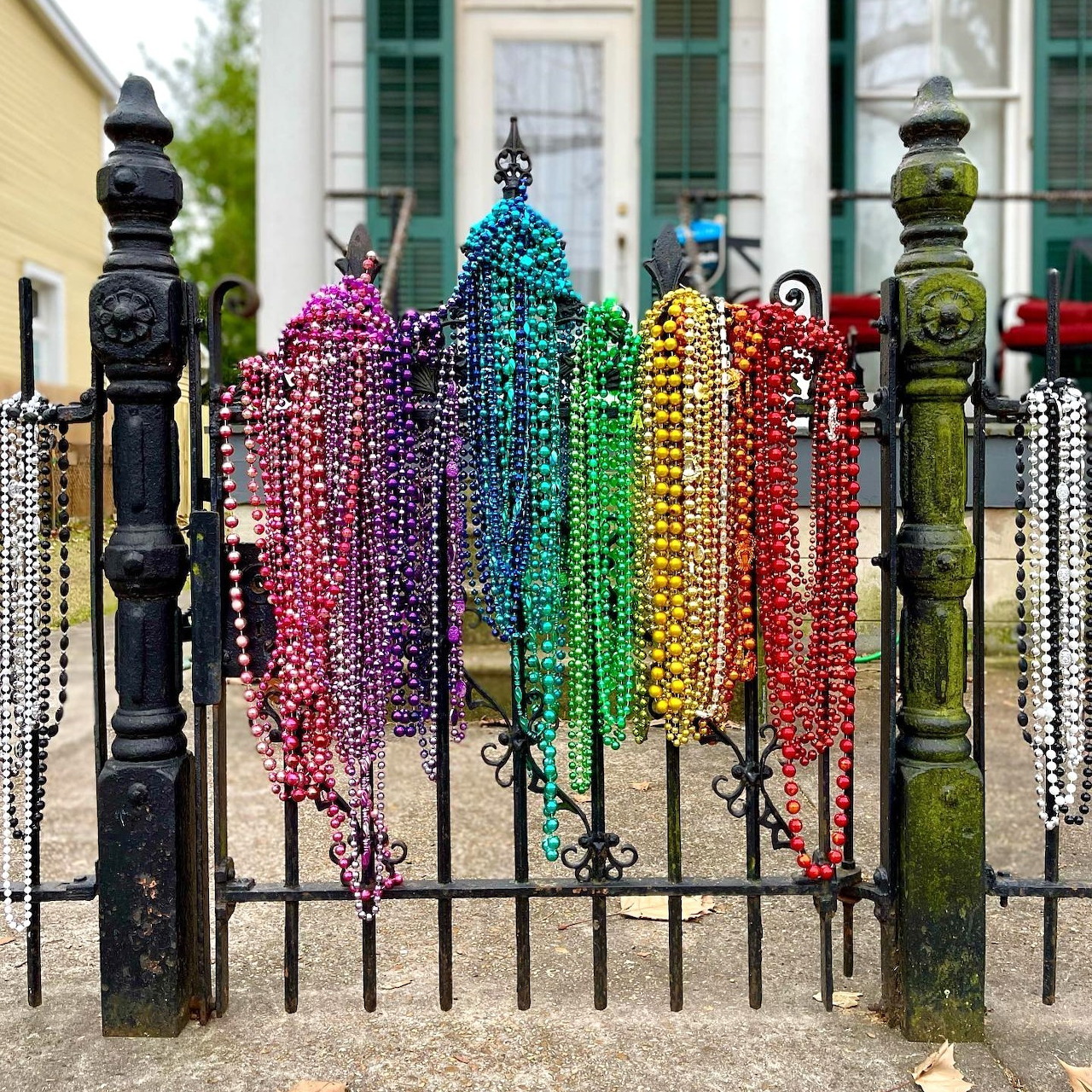 Rainbow colored beaded necklaces hanging on ornate black iron fence posts