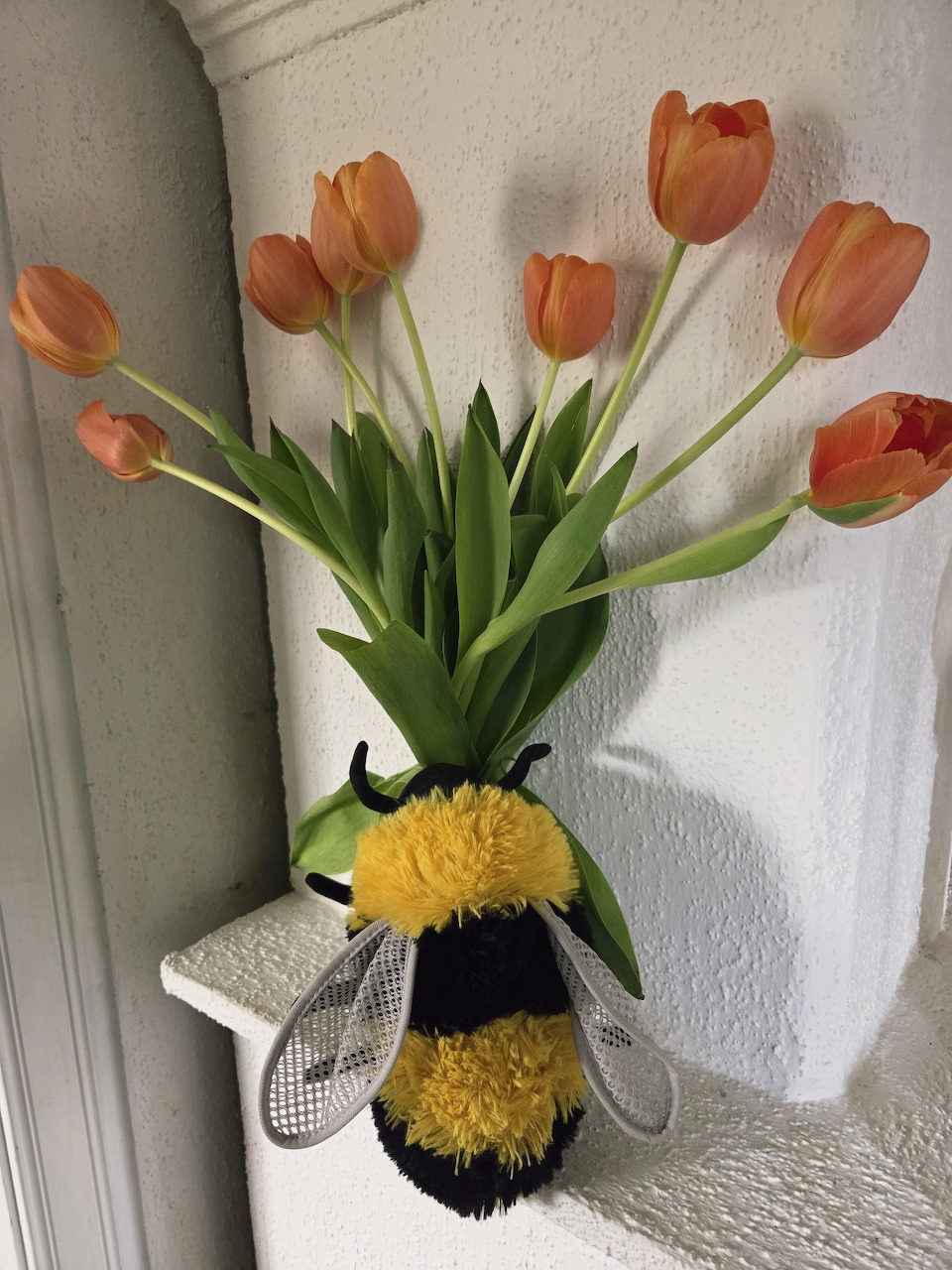 Orange tulips arranged in a plush bumblebee vase on a white shelf