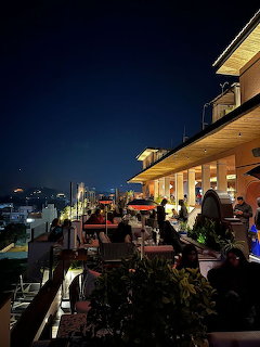 Rooftop cafe at night with people, warm lighting, and distant city buildings