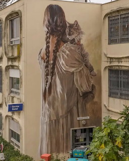 Mural of a girl with braided hair holding a cat on the side of an apartment building
