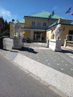 Yellow building entrance with two white lion statues on pedestals and a green roof under blue sky
