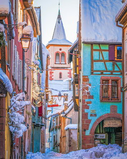 Snowy street in Alsace village with colorful traditional buildings and church tower