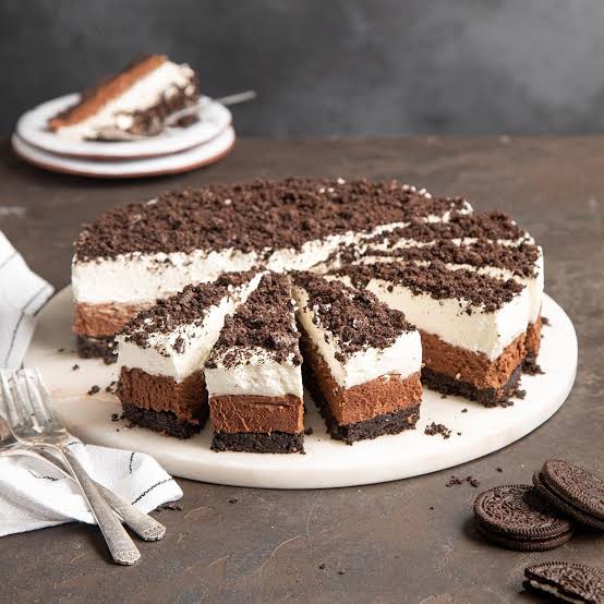 Sliced chocolate cream cake on a white plate with cookie crumbs and sandwich cookies