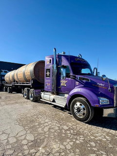 Purple semi truck carrying a large cylindrical tank on a flatbed trailer parked in an industrial area