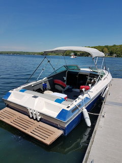 White and blue motorboat tied to a dock on a calm lake with forested hills in the background