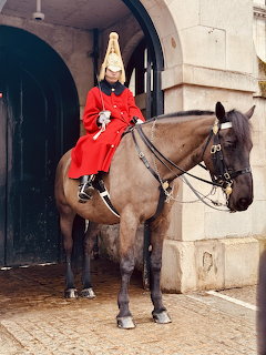 Ceremonial guard in red uniform mounted on brown horse at Horse Guards building entrance with stone archway