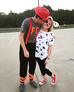 Couple kissing in matching Halloween costumes, firefighter and dalmatian theme, standing on outdoor pavement