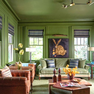 Green living room with paneled walls, sofas, leather chairs, windows, and a coffee table