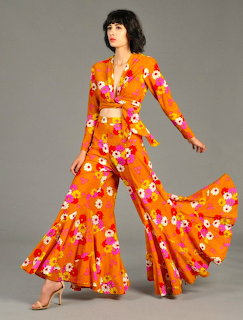 Woman in orange floral bell-bottom outfit with dramatic flared pants posing against gray background