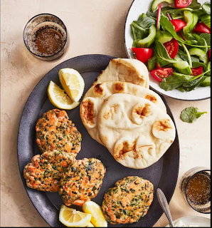 Salmon burgers on dark plate with flatbread, lemon, and side salad on beige background