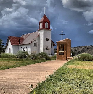 White church with red roof and steeple under dark storm clouds, green grass and pathway leading to entrance