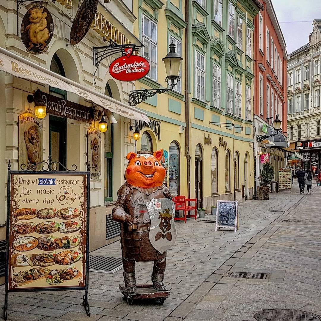 Colorful historic buildings with cafes and a decorative bear statue on a pedestrian street in Bratislava old town