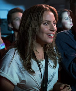 Smiling woman with long brown hair seated in a dimly lit audience