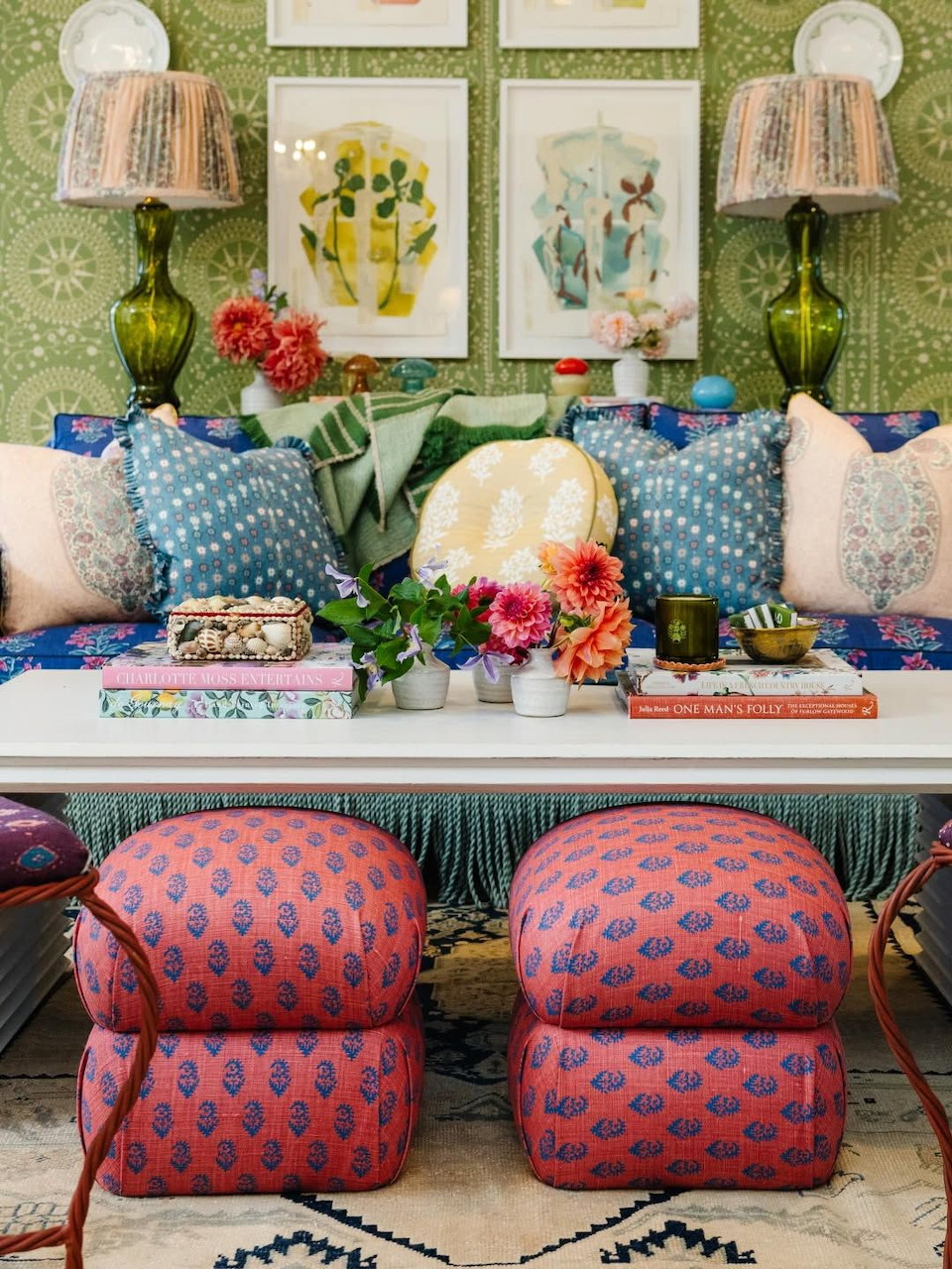 Colorful living room with patterned ottomans, pillows, flowers, framed art, and green lamps