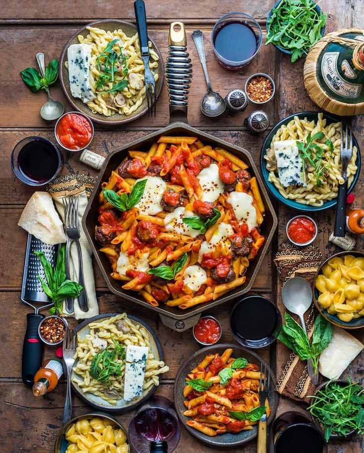 Overhead shot of a wooden table covered with various Italian pasta dishes, sauces, wine, and fresh ingredients