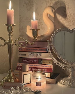 Lit candles in ornate holders next to vintage books, ornate mirror, and pearls on decorated table