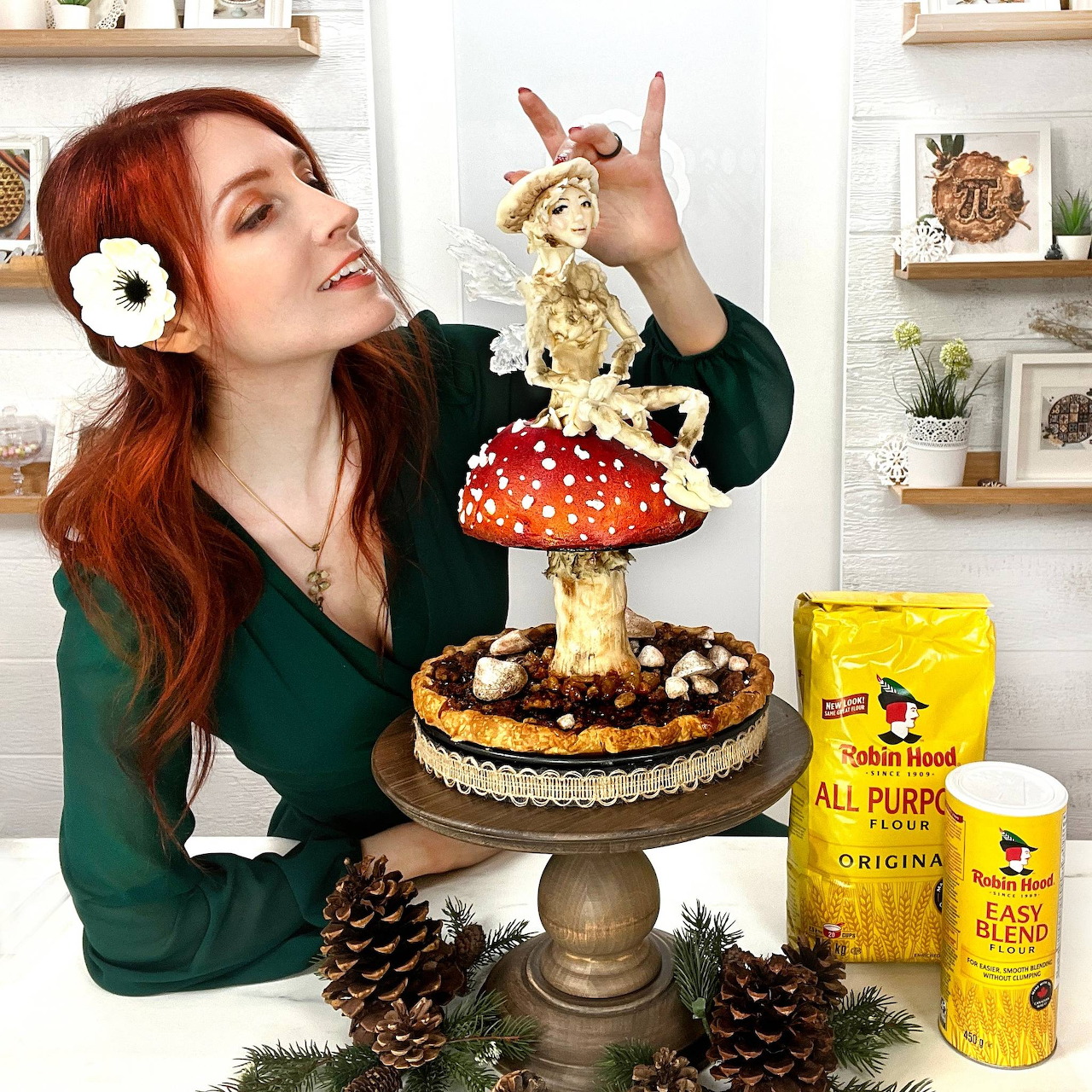 Red-haired woman posing with a mushroom-shaped cake covered in frosting on a stand