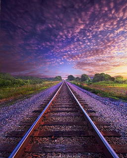 Railroad tracks leading to the horizon under a vivid purple and pink sunset sky with scattered clouds