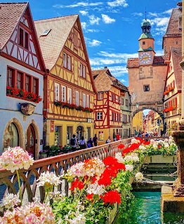 Historic Bavarian village with colorful half-timbered houses, blooming flowers along canal, and clock tower