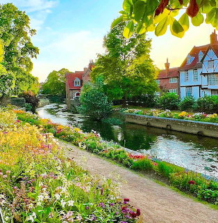English village canal with colorful flower gardens, green trees, and traditional houses along the water