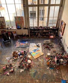 Aerial view of messy artist studio floor with paints, canvases, and art supplies